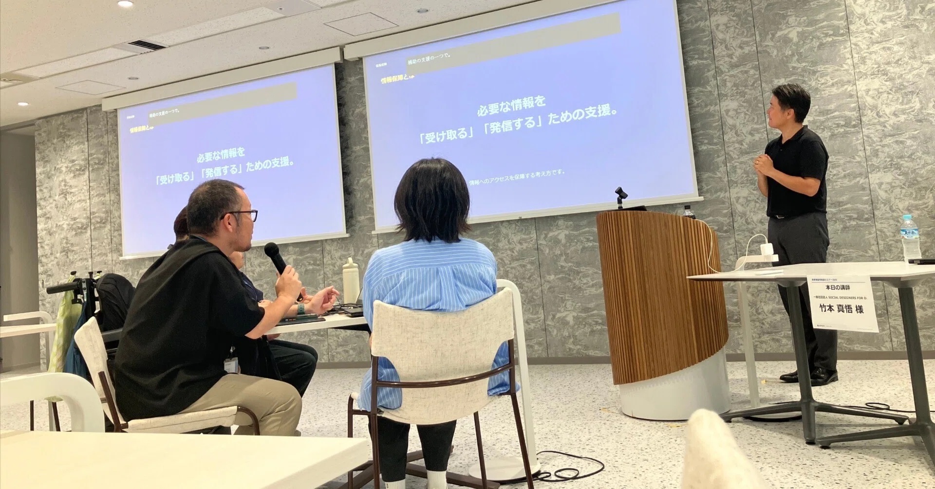 講演の様子。スクリーンの前で講師が話し、手前で参加者が聞いている